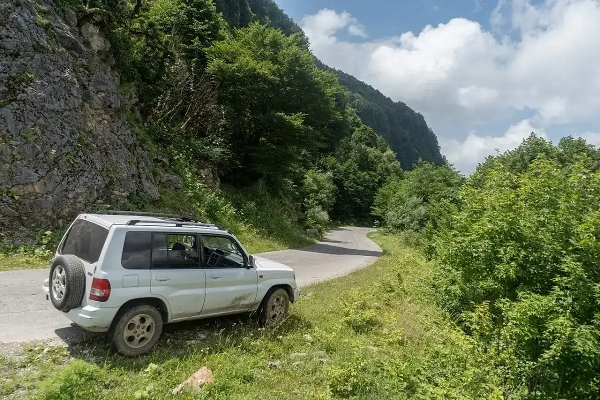 White SUV parked on a narrow mountain road between rock and forest in Georgia
