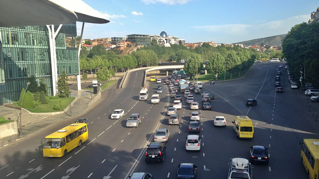 Heavy traffic and yellow minibuses on a multi-lane avenue by the Public Service Hall in Tbilisi, the Presidential Palace dome on the hill behind