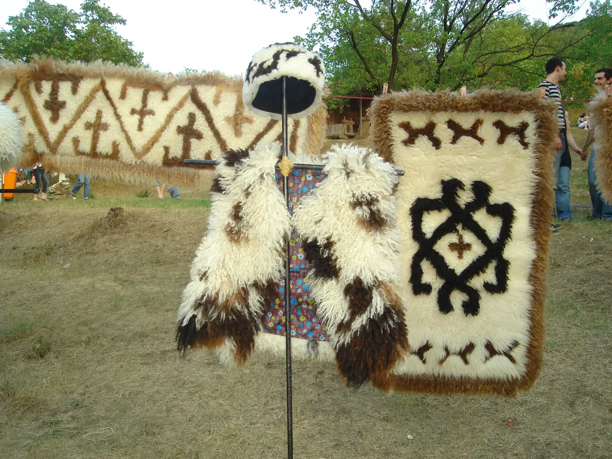 Felted wool cloaks and a shaggy hat hanging on a rail with patterned rugs behind