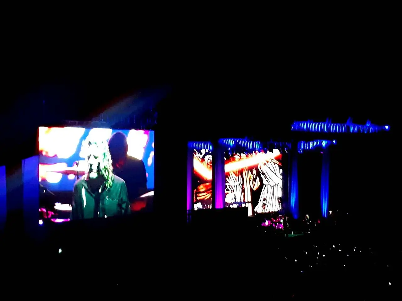 Night stage with big screens showing a long-haired singer, lit in blue and red