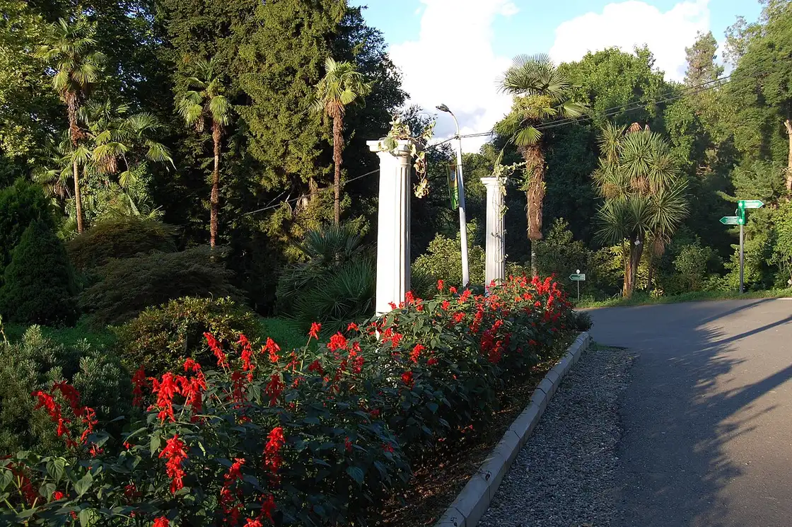 A white pergola and a flowerbed with red flowers along a garden path