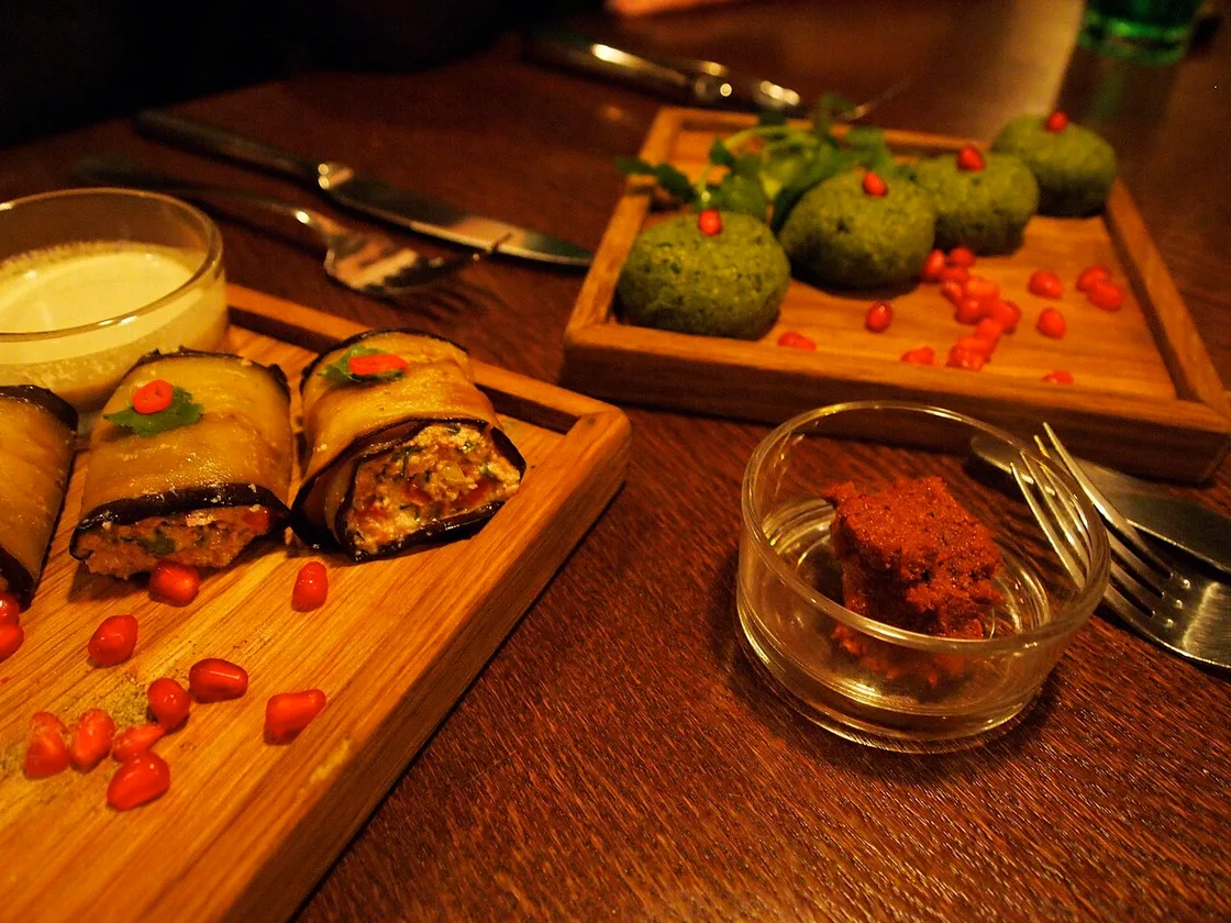 A plate of pkhali balls and badrijani aubergine rolls with pomegranate seeds, and a bowl of ajika
