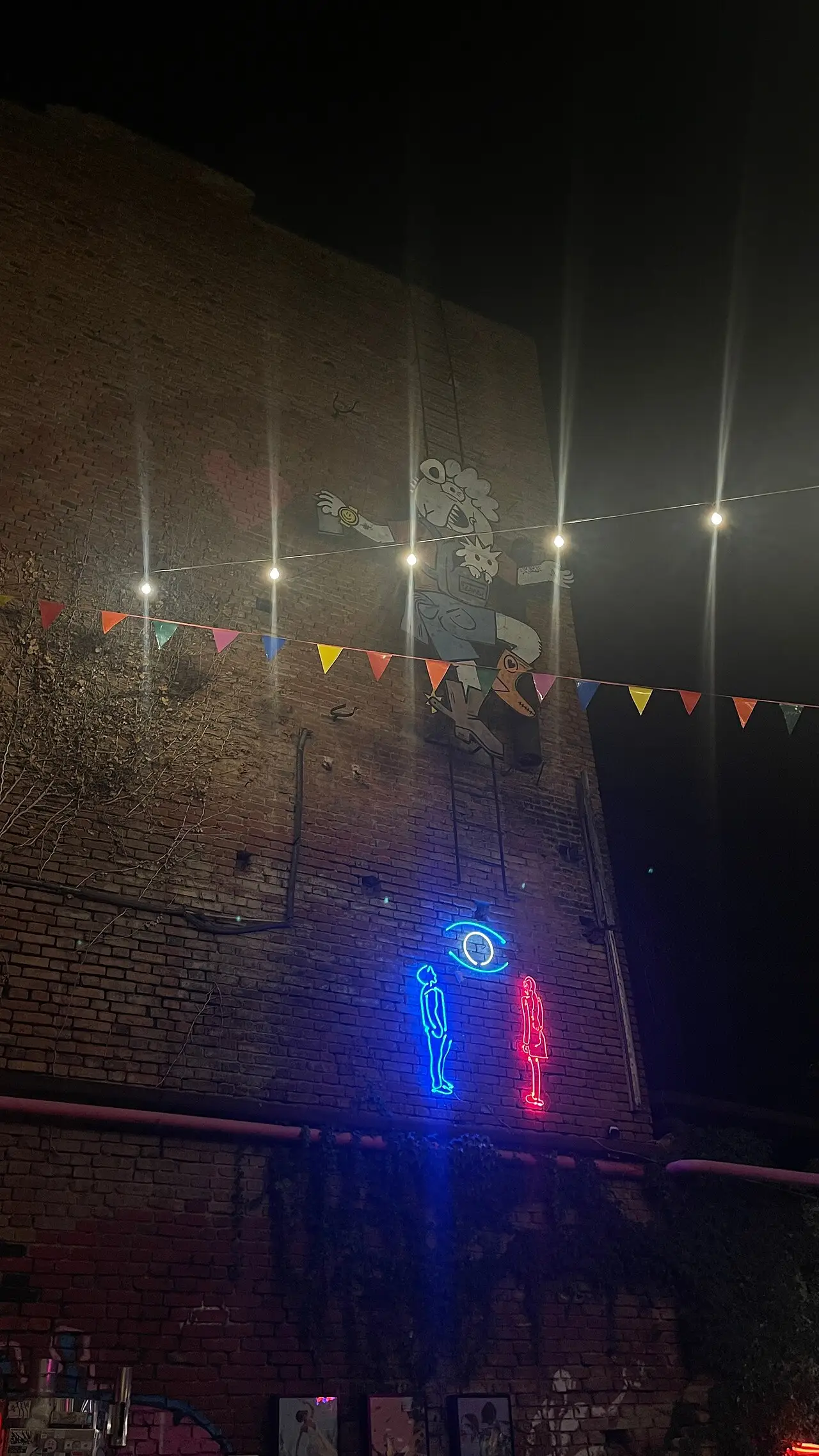 Street art and neon figures on a brick wall of Fabrika in Tbilisi at night