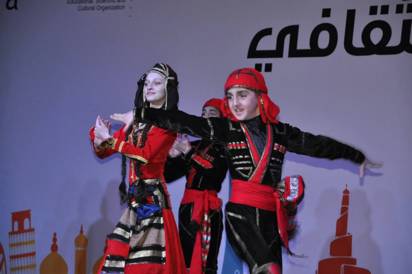 A man and a woman in red and black costumes dancing the Acharuli on stage