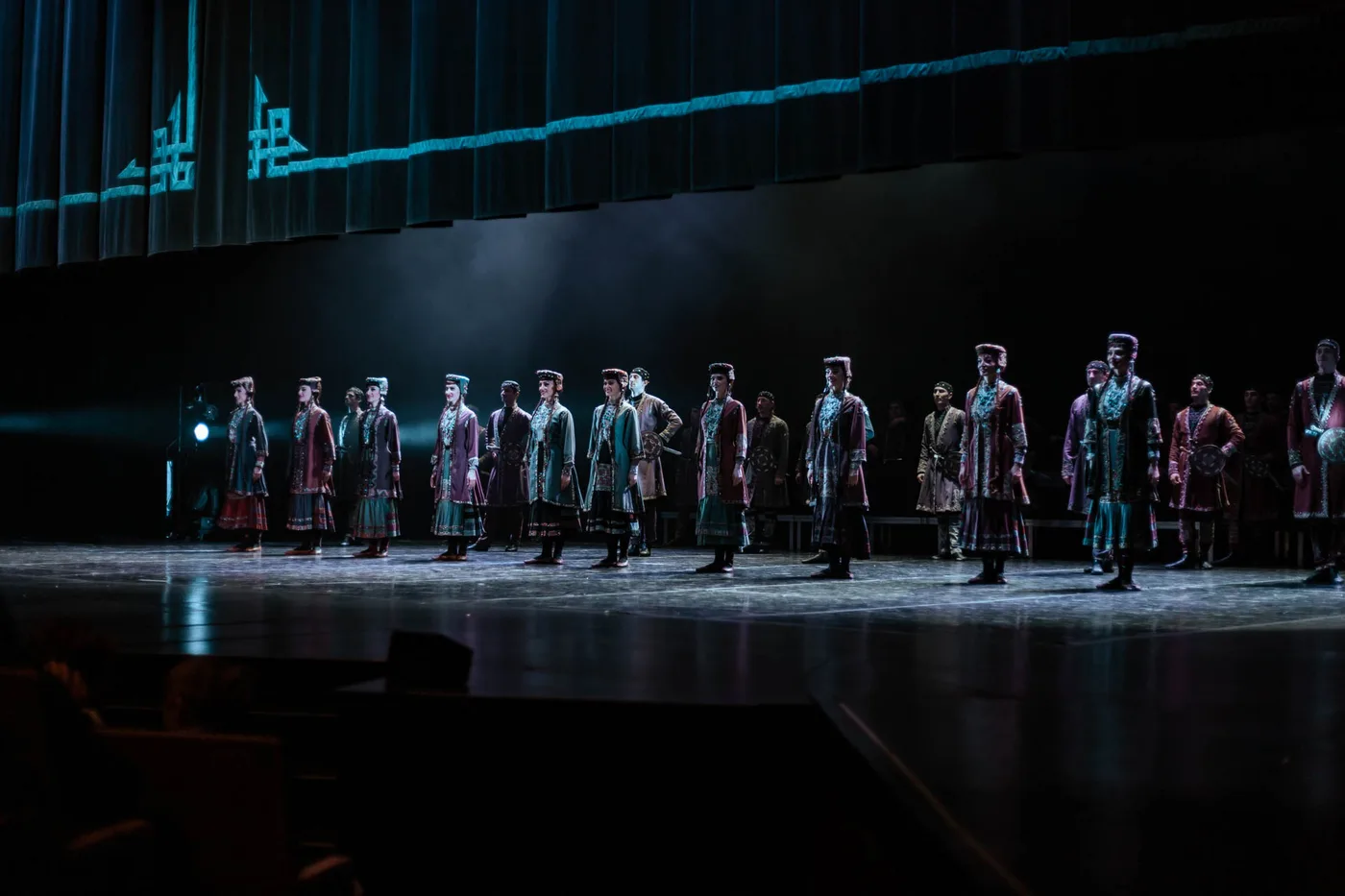 Sukhishvili dancers in dark folk costumes across a darkened stage