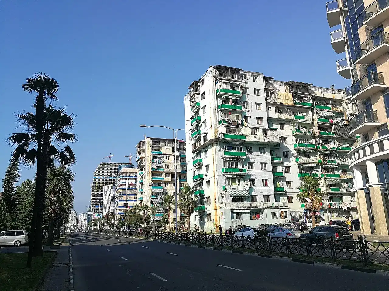 Residential apartment blocks with balconies and palm trees along a Batumi boulevard, high-rises under construction in the background