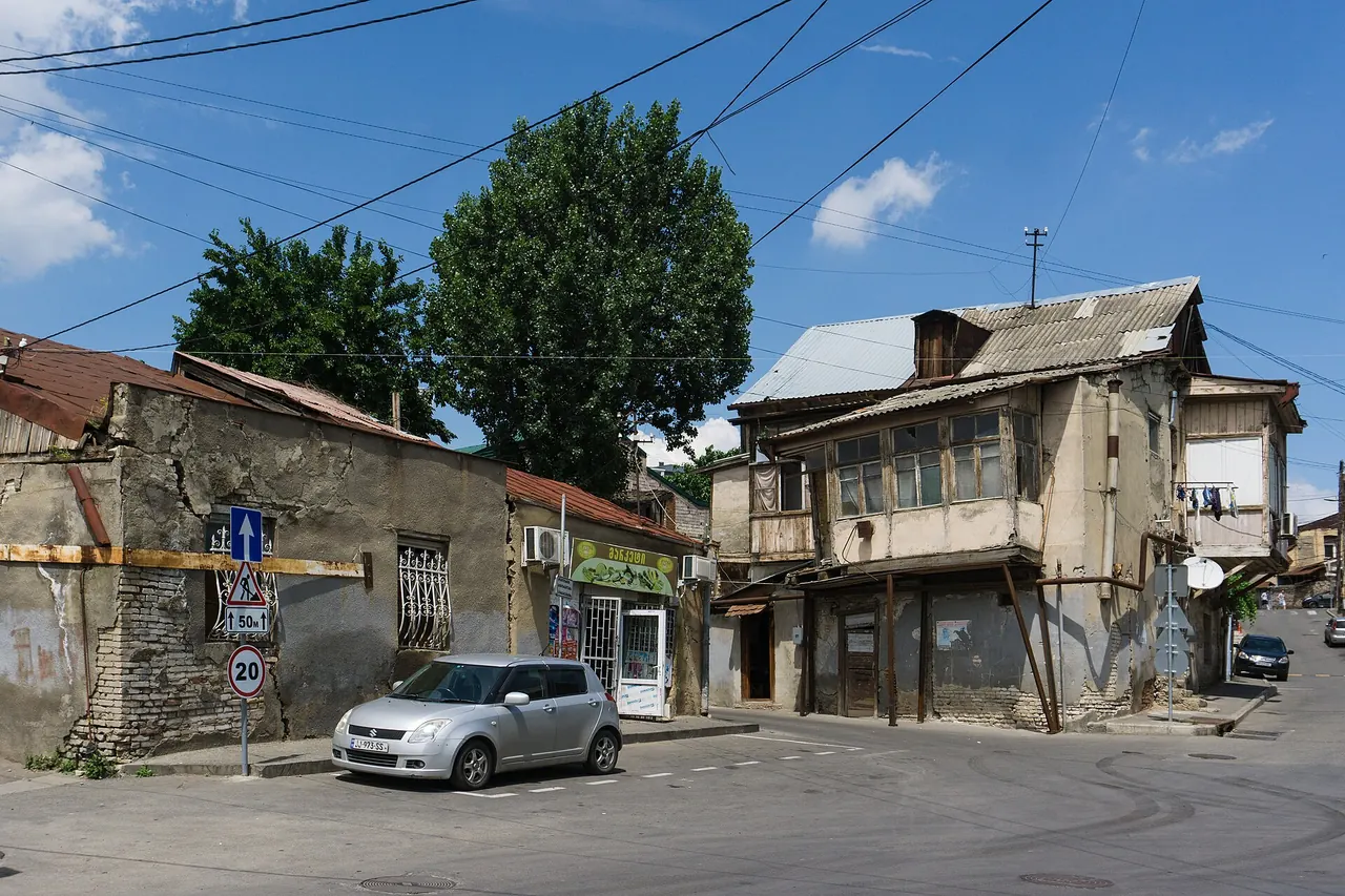 A street corner in Avlabari with old low houses, a wooden balcony and a small shop