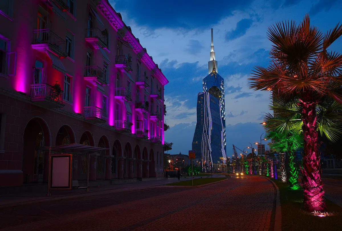 A lit-up high-rise tower and an evening street in New Batumi
