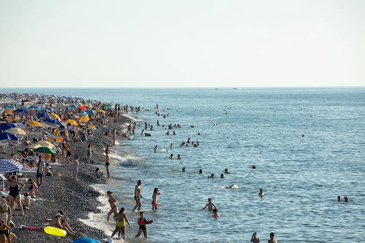 Packed pebble beach in Batumi with umbrellas and swimmers at the height of the season