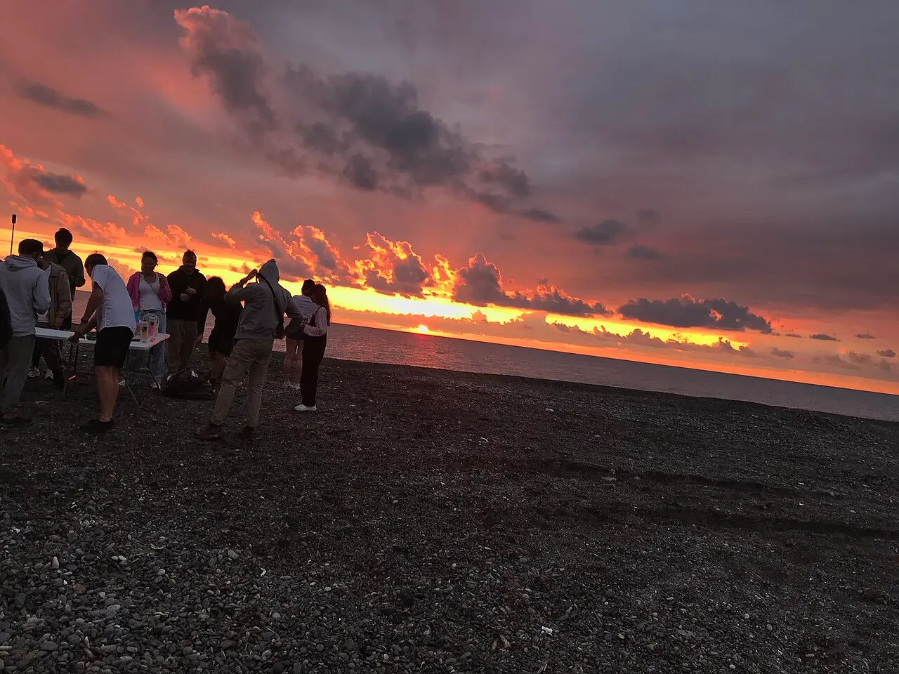Sunset over the sea at Kobuleti, people standing on dark pebbles by the water