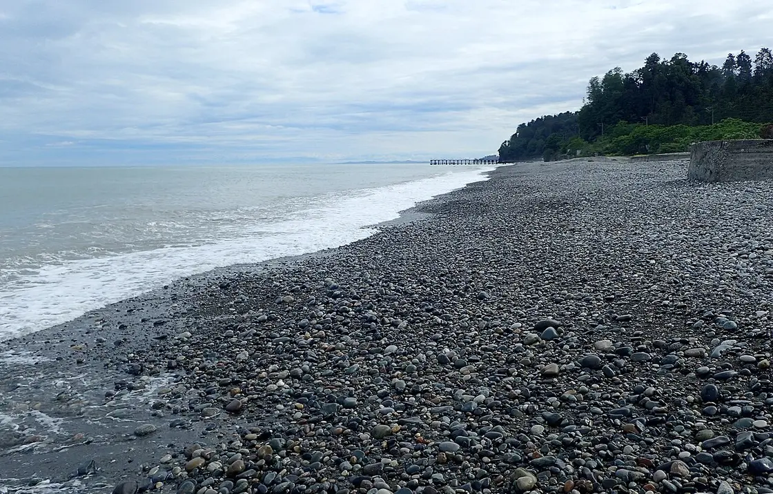 Empty pebble beach at Green Cape under a grey sky, with a pier in the distance