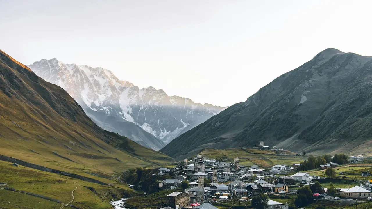 A Svaneti valley with a mountain village and a snowy peak at dawn