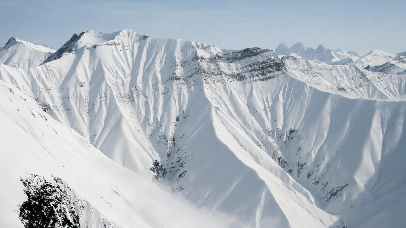 Snow-covered ridges of the Greater Caucasus near Gudauri in winter: sharp slopes in fresh snow and jagged peaks far on the right