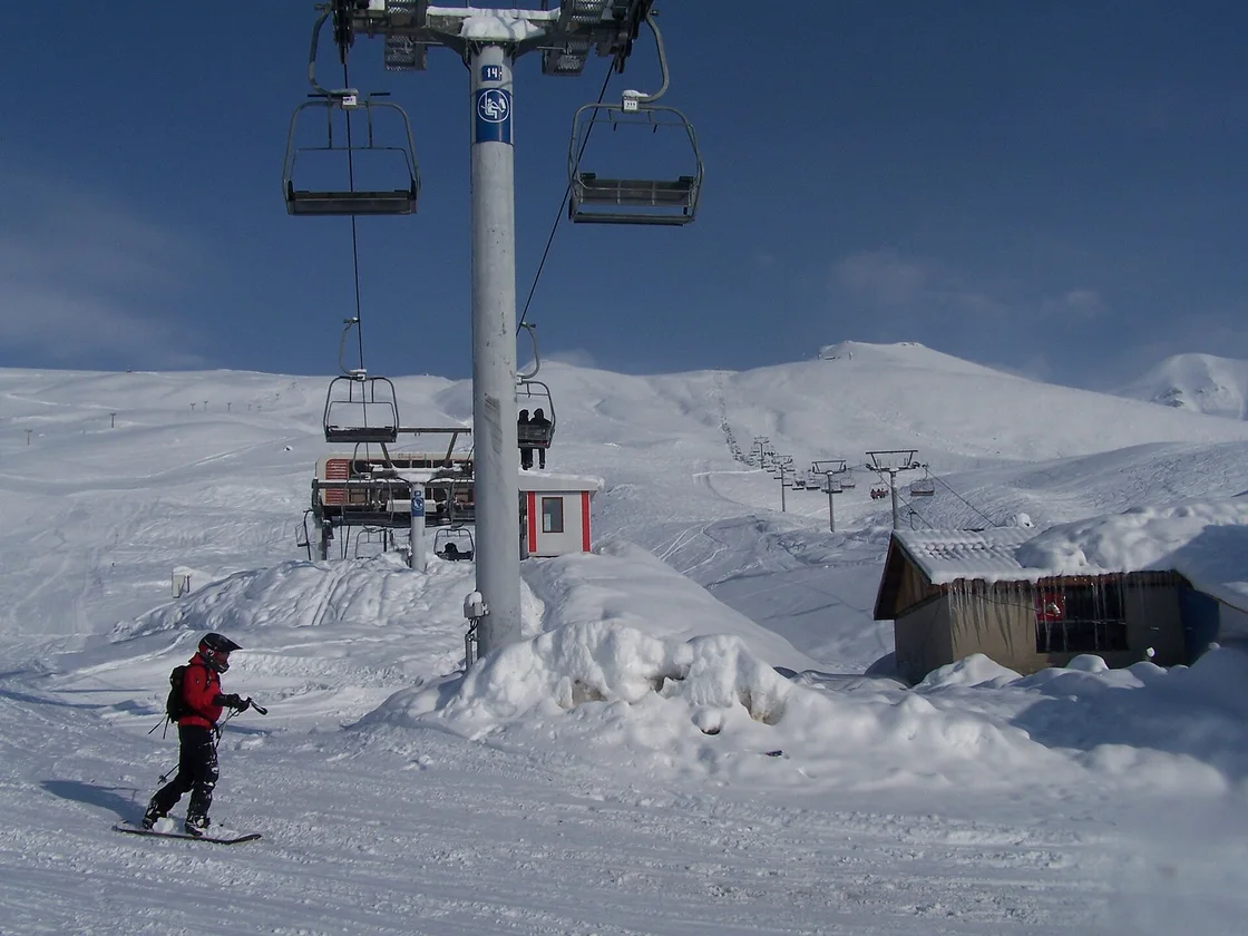 A chairlift over a snowy Gudauri slope with a snowboarder in a red jacket in the foreground