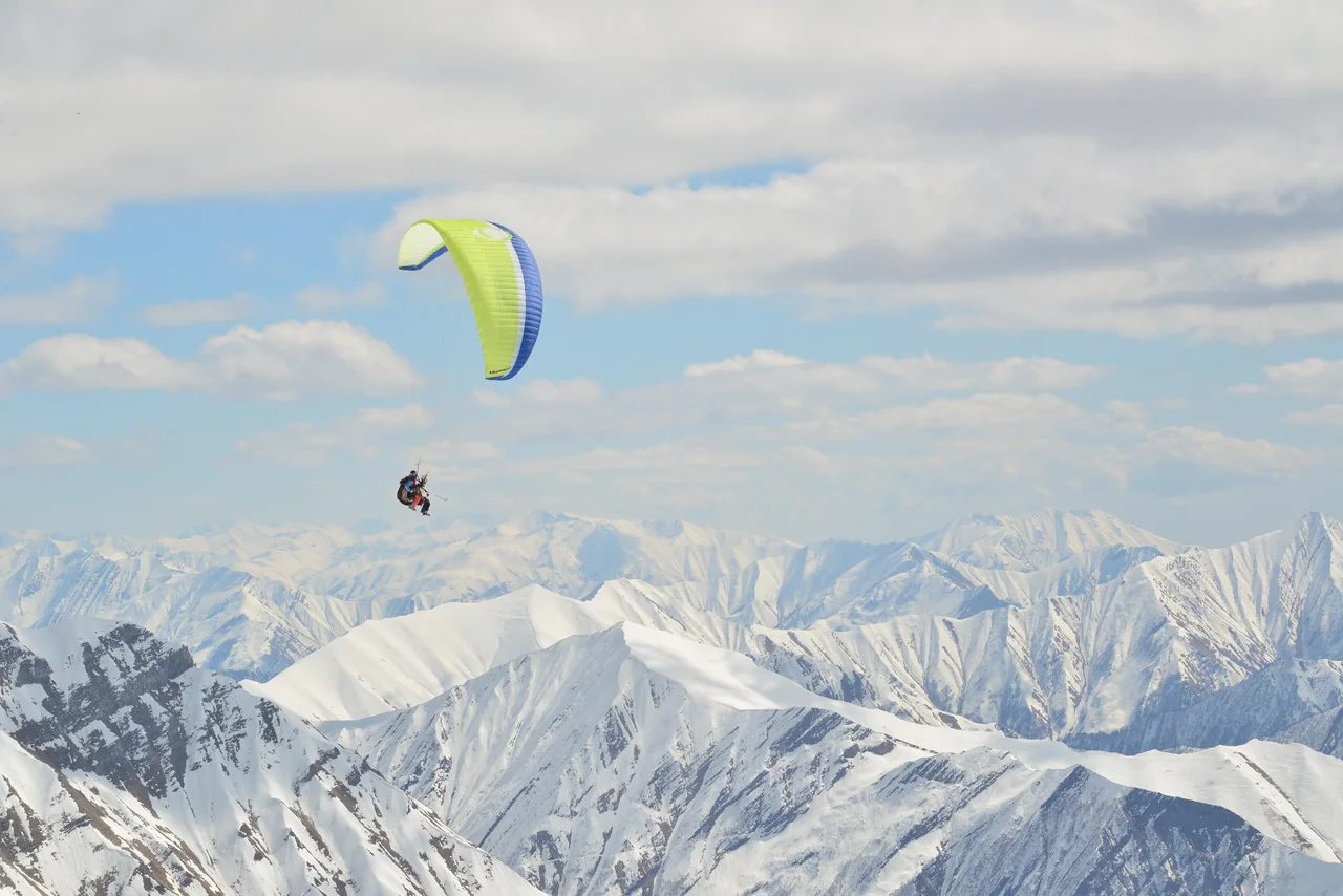 A tandem wing against a blue sky with the snowy Greater Caucasus below