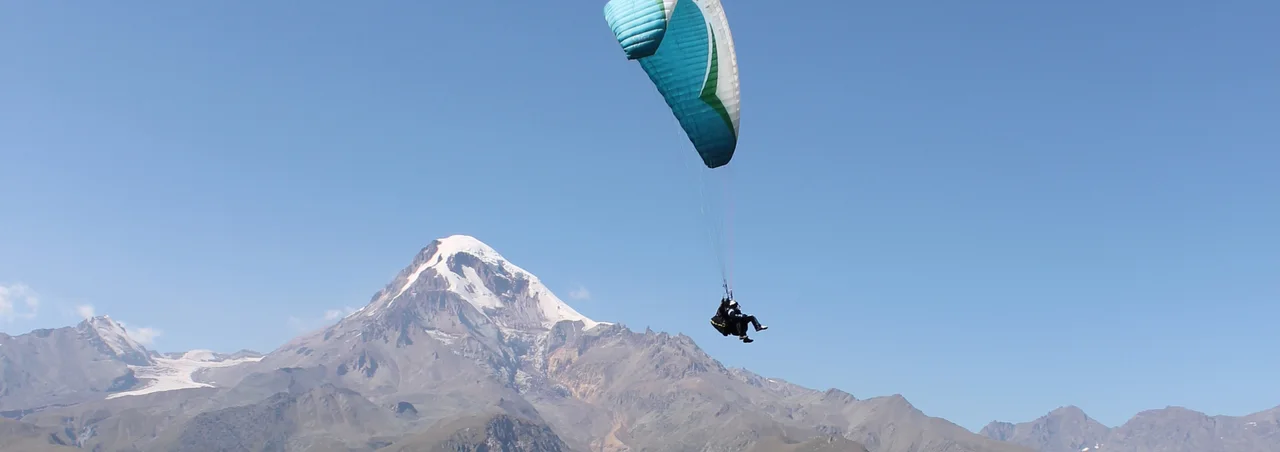 A tandem paraglider with Mount Kazbek on the horizon