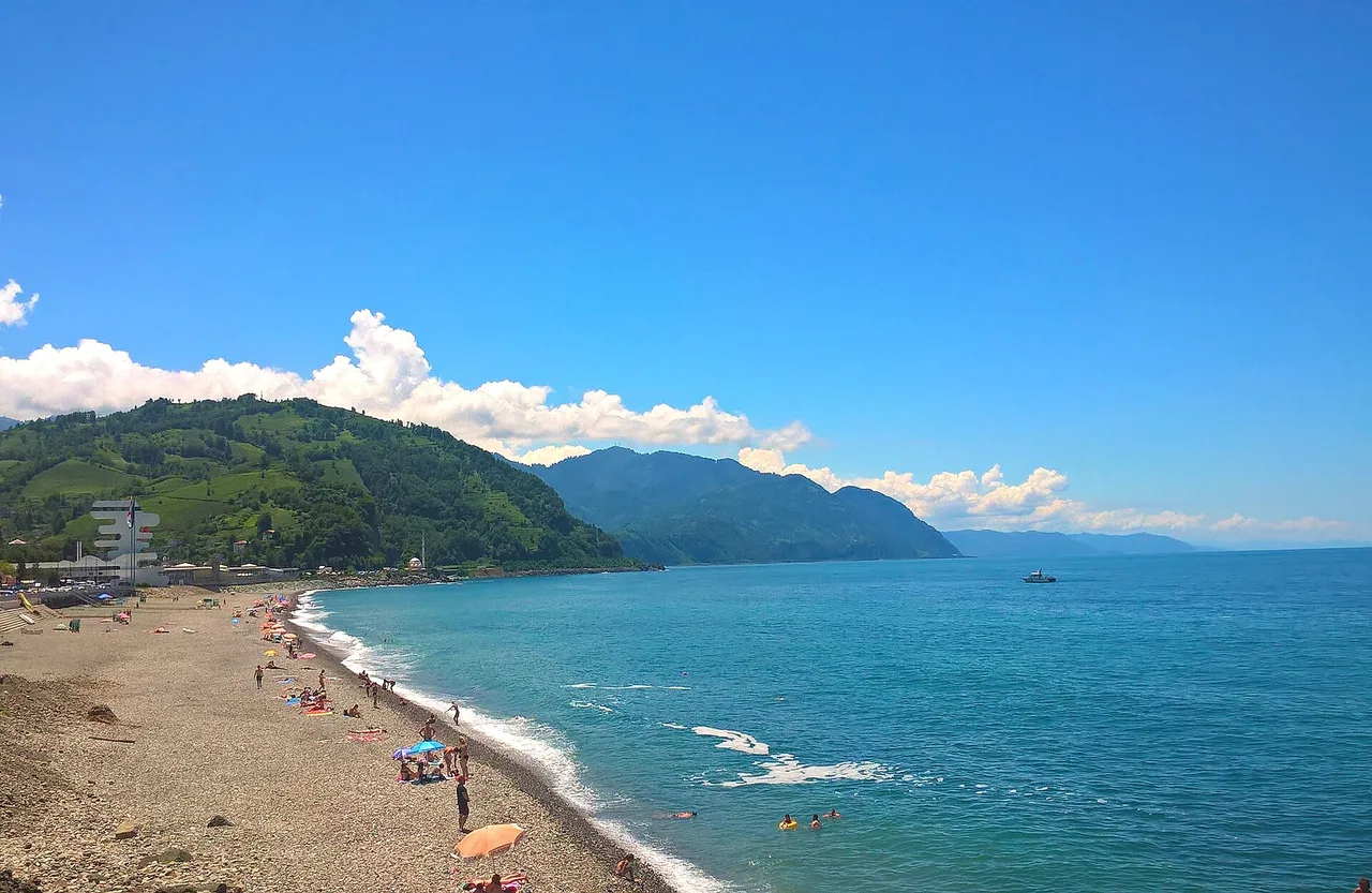 A sunny pebble beach and the blue Black Sea below the green hills of Adjara