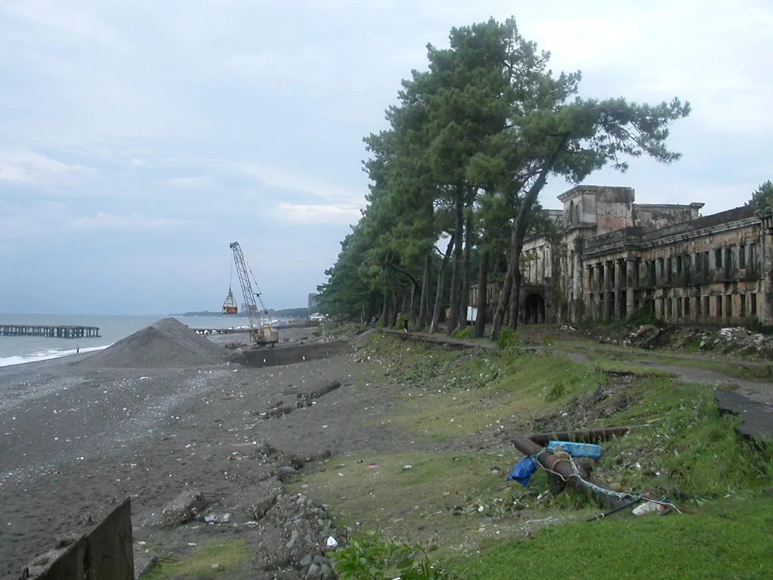The dark pebble shore of Kobuleti and the ruins of an old sanatorium among pines