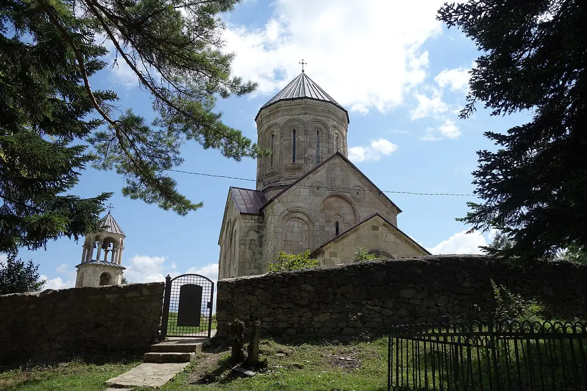 The domed Nikortsminda cathedral with its bell tower behind a stone wall