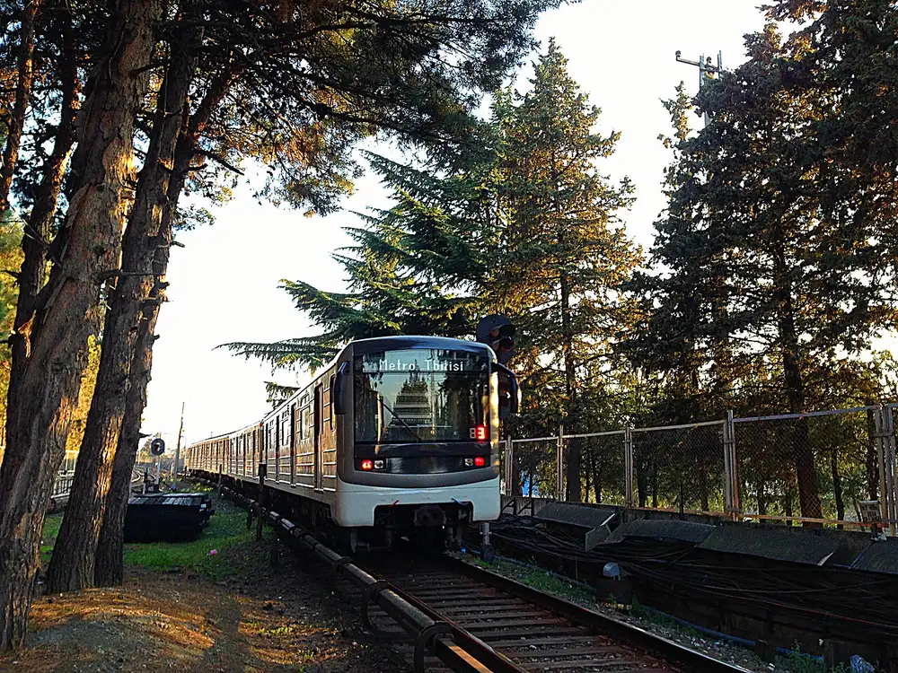 A Tbilisi metro train on an open-air stretch of track among trees
