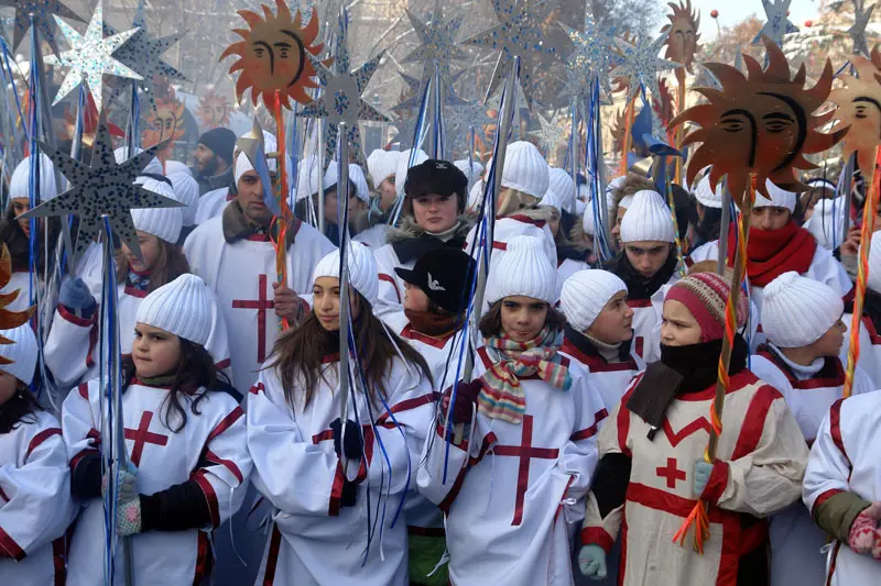 Children in white capes with crosses and coloured star poles in a Christmas procession