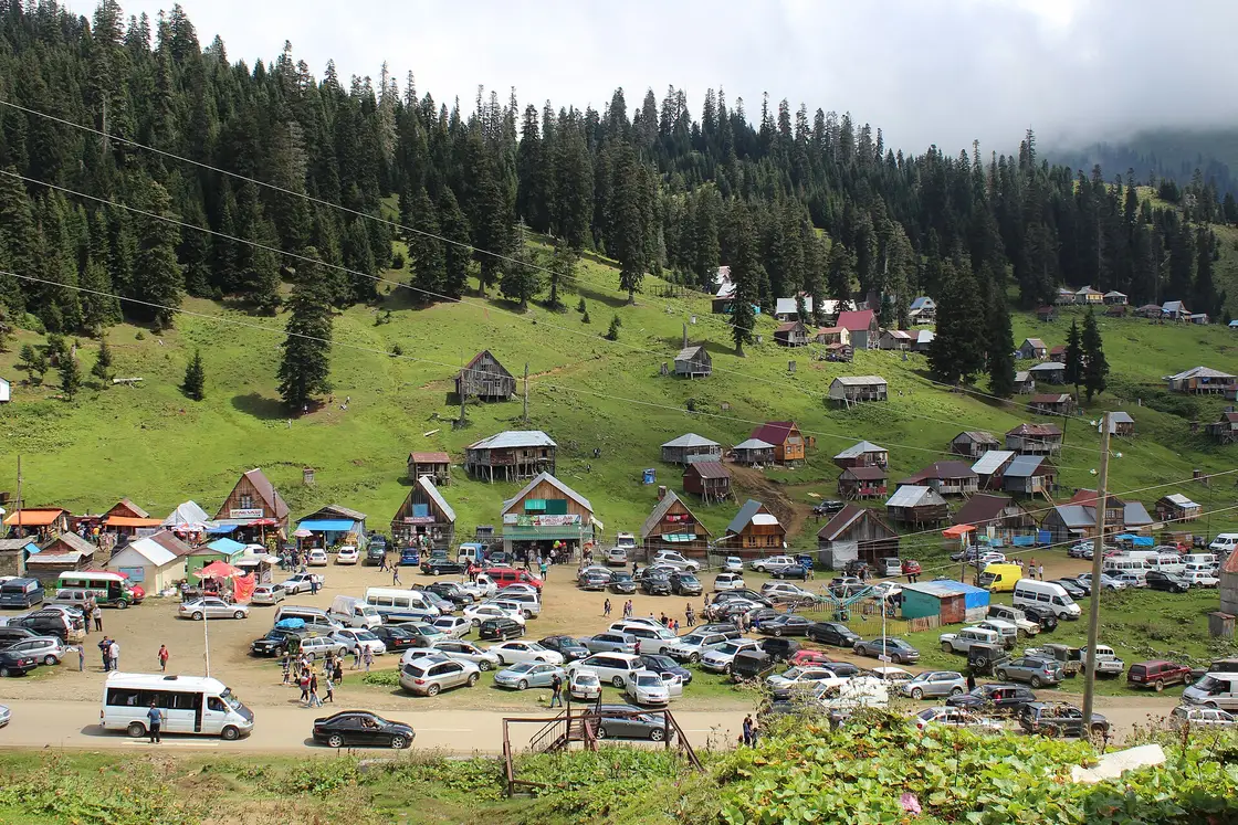 Mountain village of timber houses on stilts above a meadow with a field full of parked cars