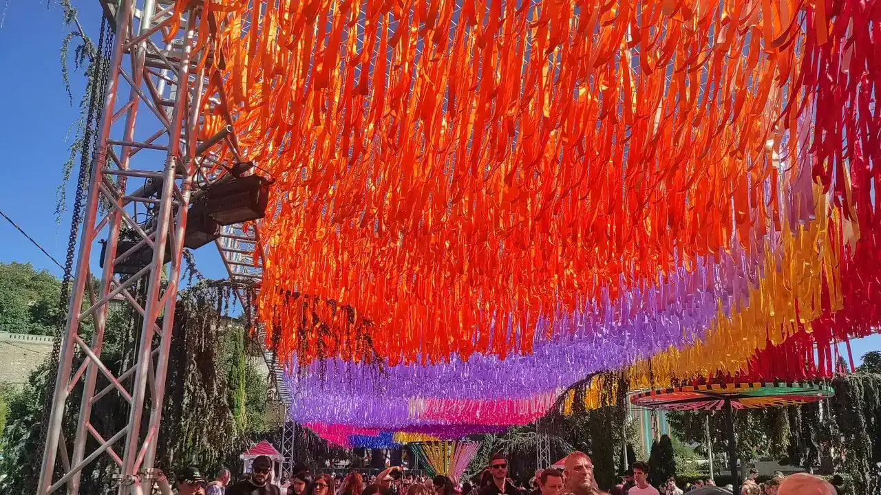 Canopy of coloured ribbons over a Rike Park walkway with a crowd underneath at Tbilisoba