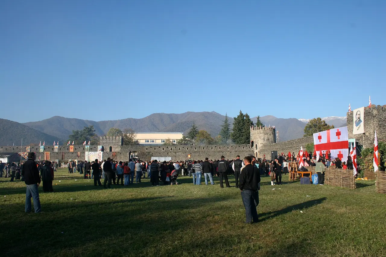 Crowd with Georgian flags inside the fortress walls at Kvareli, mountains behind