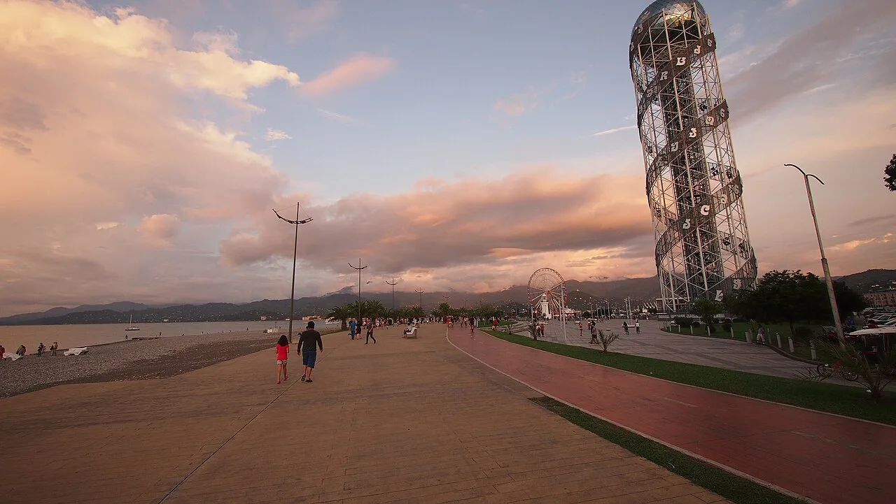 Batumi boulevard at sunset: the Alphabet Tower, a Ferris wheel and people walking by the sea
