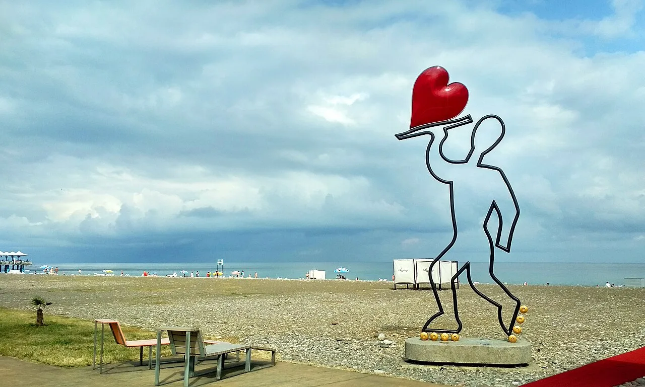 Batumi beach under heavy grey cloud cover, a roller-skater heart sculpture in the foreground