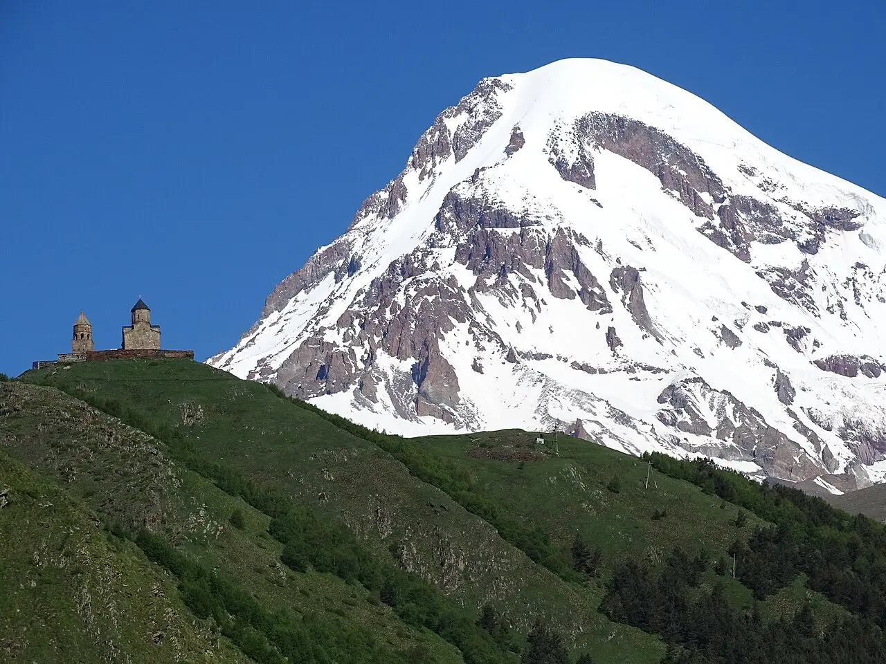 Gergeti church on a green hilltop ridge, with snow-capped Kazbek rising behind
