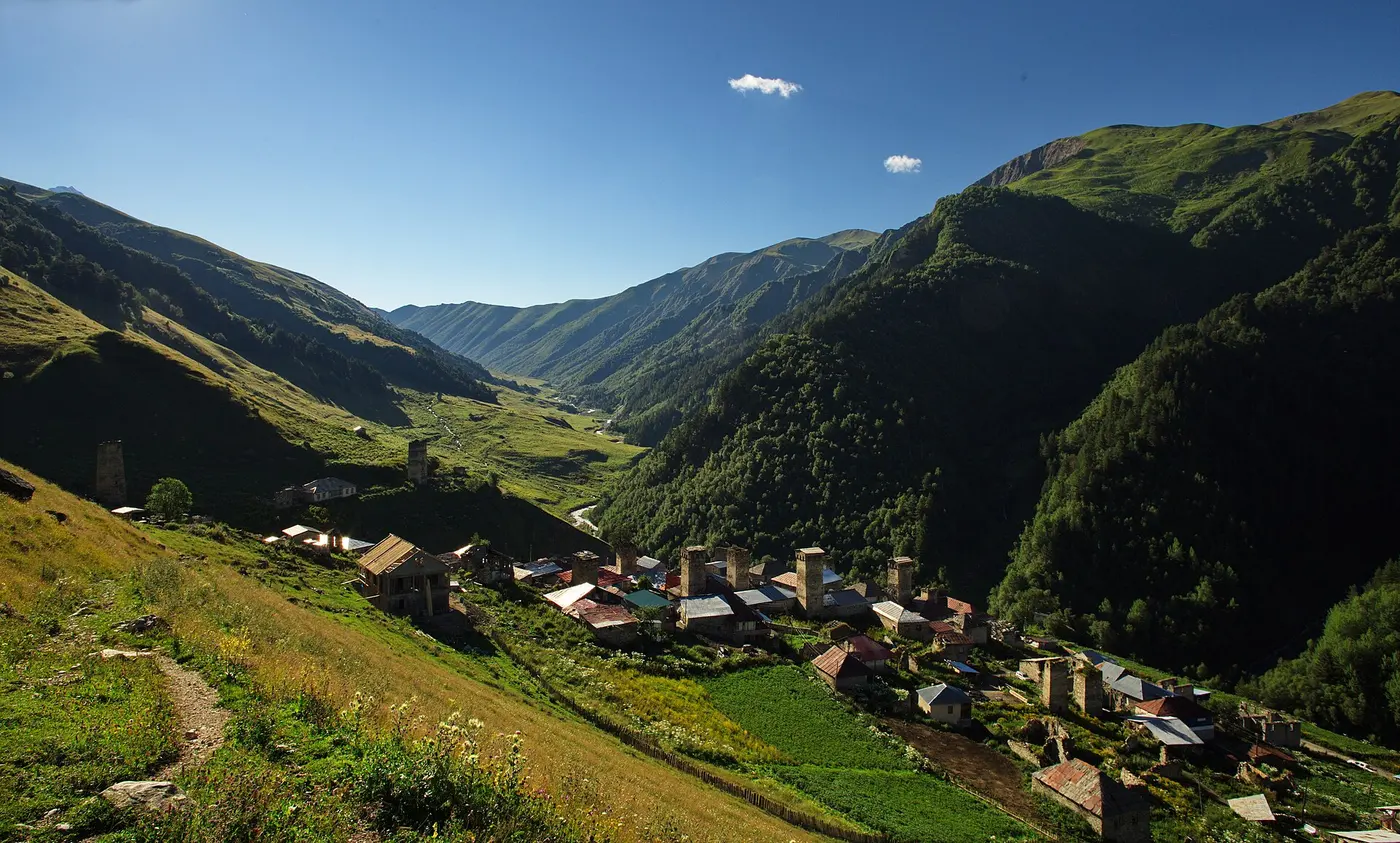 The village of Adishi with stone towers in a green valley, a trail in the foreground