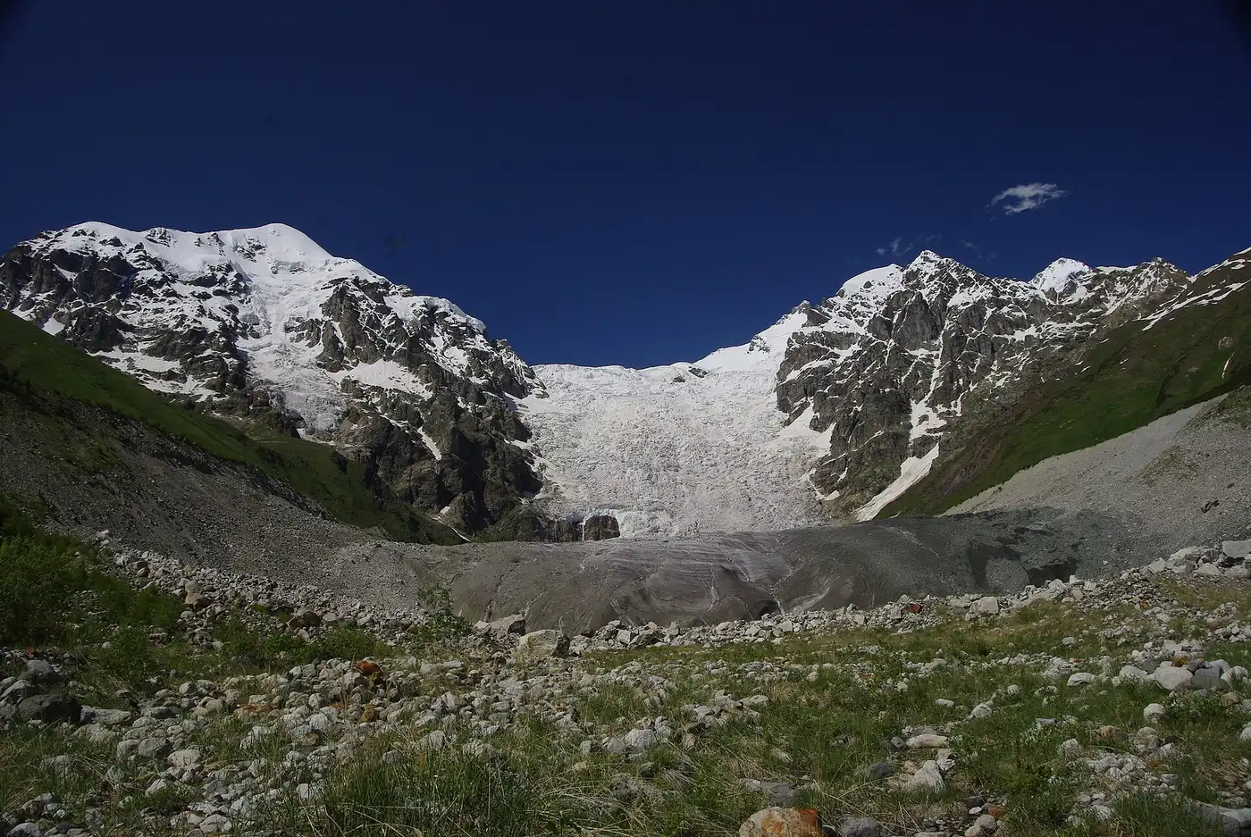 The Adishi Glacier spilling between snowy peaks above a stony valley
