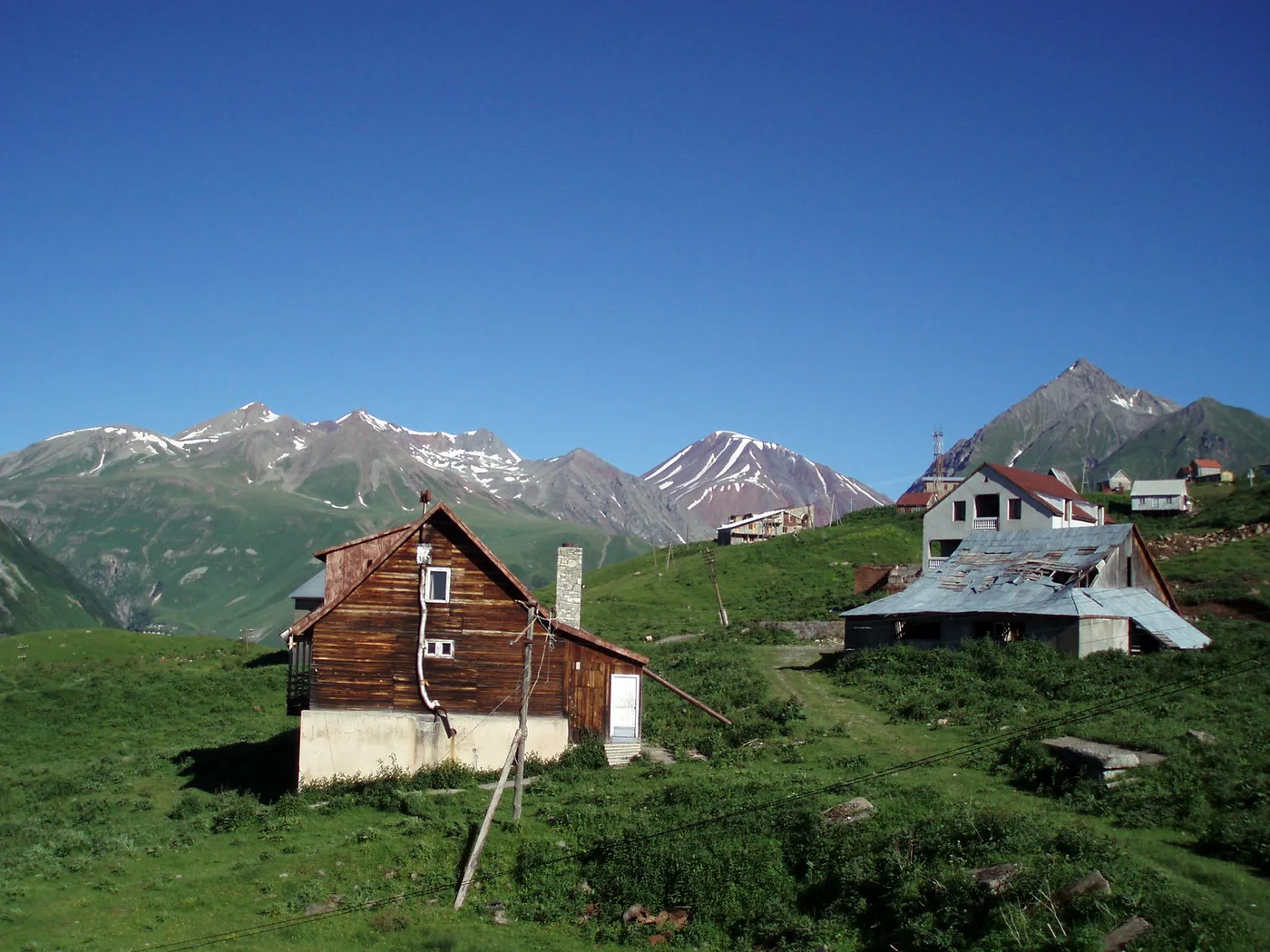 Houses of Gudauri on a green slope against snowy peaks